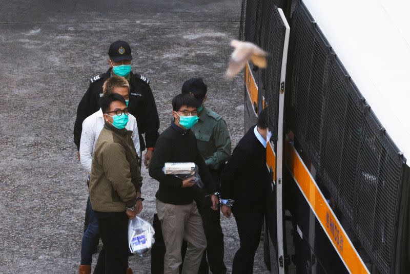 A bird flies in front of pro-democracy activists Ivan Lam and Joshua Wong as they walk to a prison van to head to court, after pleading guilty to charges of organising and inciting an unauthorised assembly near the police headquarters