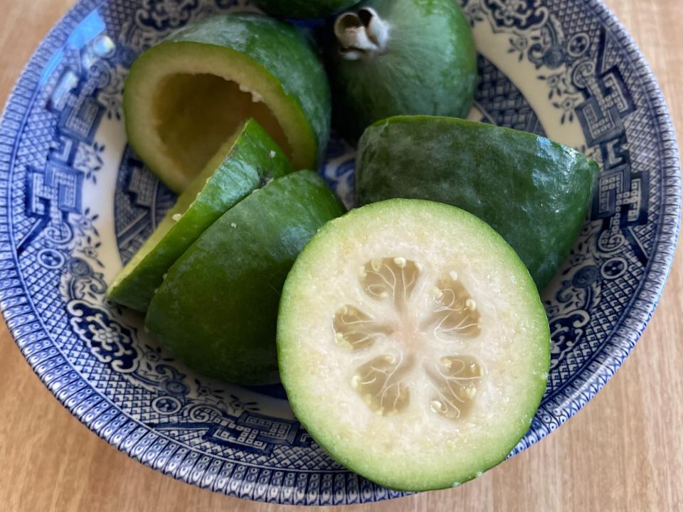 Halved feijoa fruits, which look like limes on the outside with cucumber-like centers, in a blue-and-white bowl