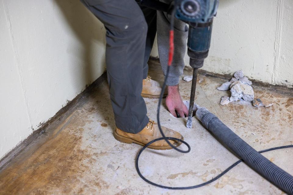 A worker is making a hole in the basement floor to install a radon mitigation system.