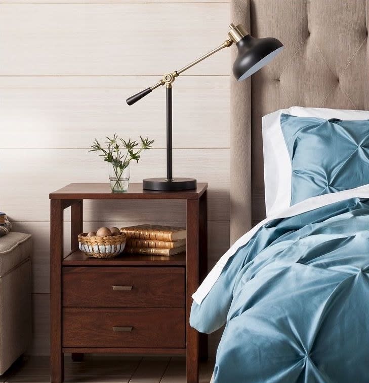 Bedside table with lamp, decorative plant, and bowls; adjacent to a bed with blue bedding. Ideal for bedroom decor inspiration