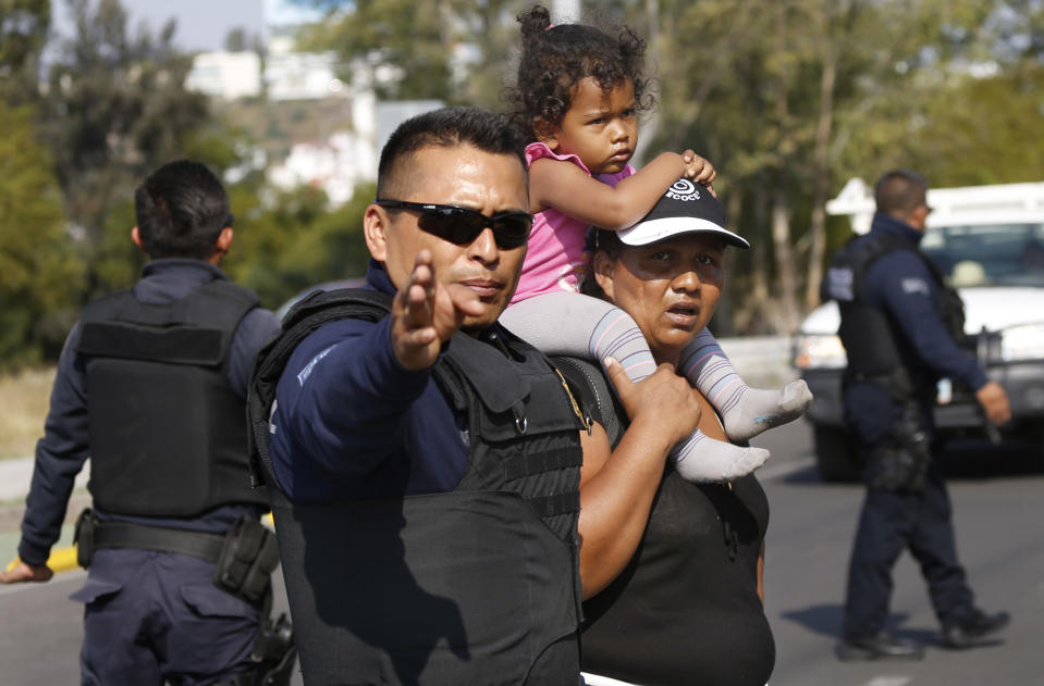 A police officer halts traffic as a Central American migrant crosses the street in Queretaro, Mexico, as they resume their journey north after leaving a temporary shelter in Mexico City, Saturday, Nov. 10, 2018. Thousands of Central American migrants were back on the move toward the U.S. border Saturday, after dedicated Mexico City metro trains whisked them to the outskirts of the capital and drivers began offering rides north. (AP Photo/Marco Ugarte)