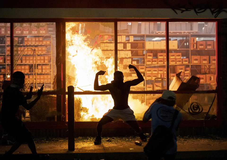 A man poses for photos in front of a fire at an AutoZone store, while protesters hold a rally for George Floyd in Minneapolis on Wednesday, May 27, 2020. Violent protests over the death of the black man in police custody broke out in Minneapolis for a second straight night Wednesday, with protesters in a standoff with officers outside a police precinct and looting of nearby stores. (Carlos Gonzalez/Star Tribune via AP)