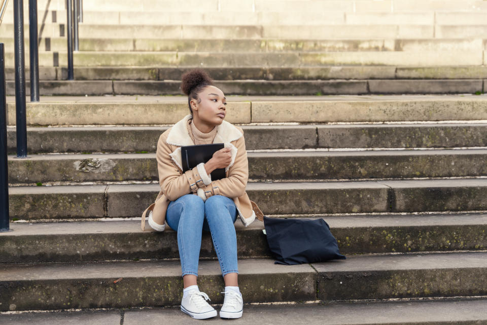 A young woman holding a book and sitting on some outside steps