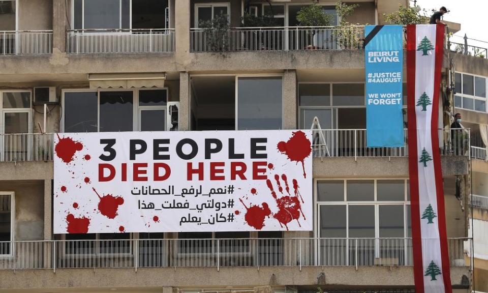 A man marks the first anniversary of the explosion on Wednesday by hanging a giant Lebanese flag on a damaged building in Beirut