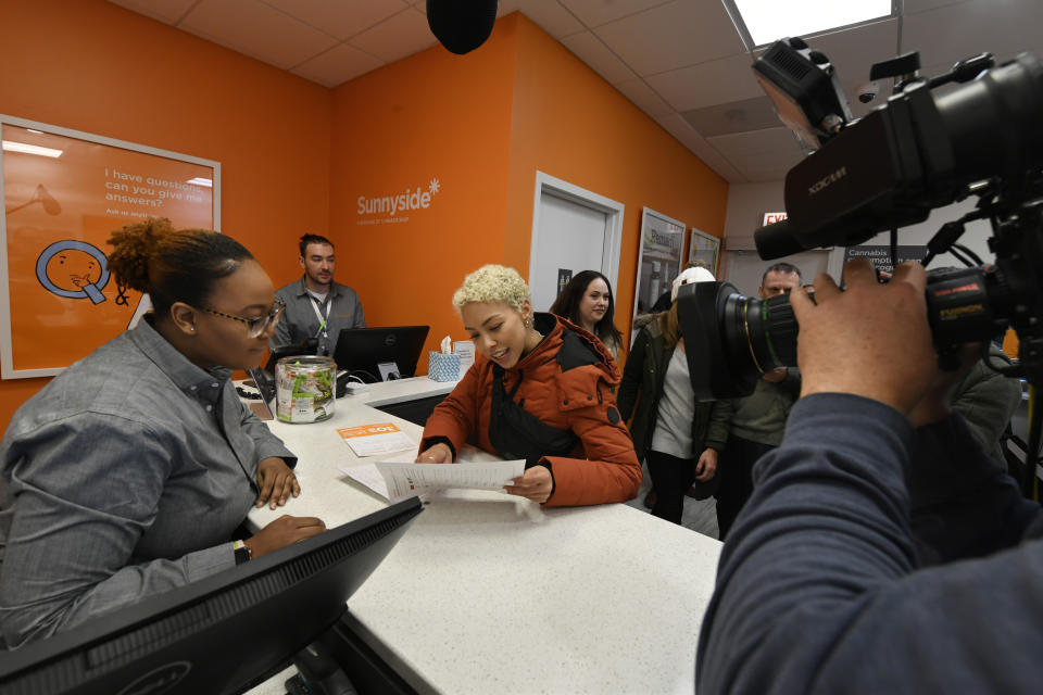 Elise Swopes, of Chicago, becomes the second person in Illinois to purchase recreational marijuana as she purchases marijuana products from employee Brea Mooney left, at Sunnyside dispensary Wednesday, Jan. 1, 2020, in Chicago. (AP Photo/Paul Beaty)