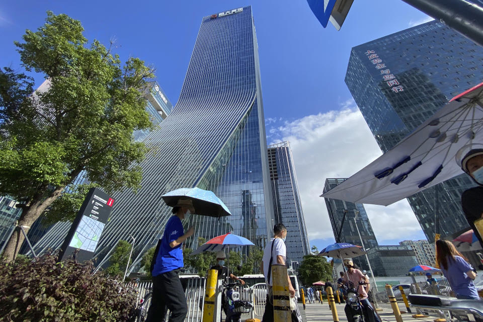 Residents pass near the headquarters for Evergrande in Shenzhen in southern China, Thursday, Sept. 23, 2021. The Chinese real estate developer whose struggle to avoid defaulting on billions of dollars of debt has rattled global markets says it will pay interest due Thursday to bondholders in China but gave no sign of plans to pay on a separate bond abroad. (AP Photo/Ng Han Guan)