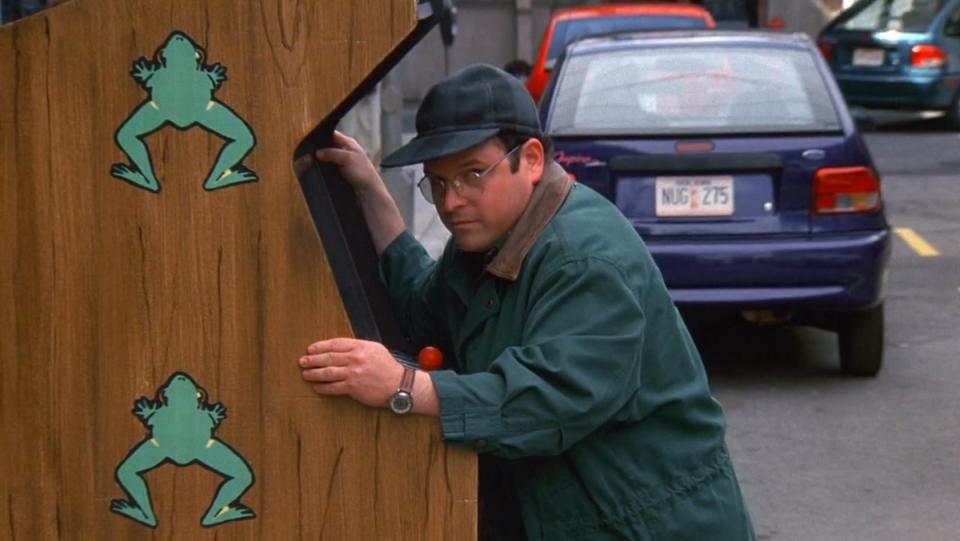 George Costanza in a baseball cap pushing a Frogger arcade machine on a New York City street from Seinfeld