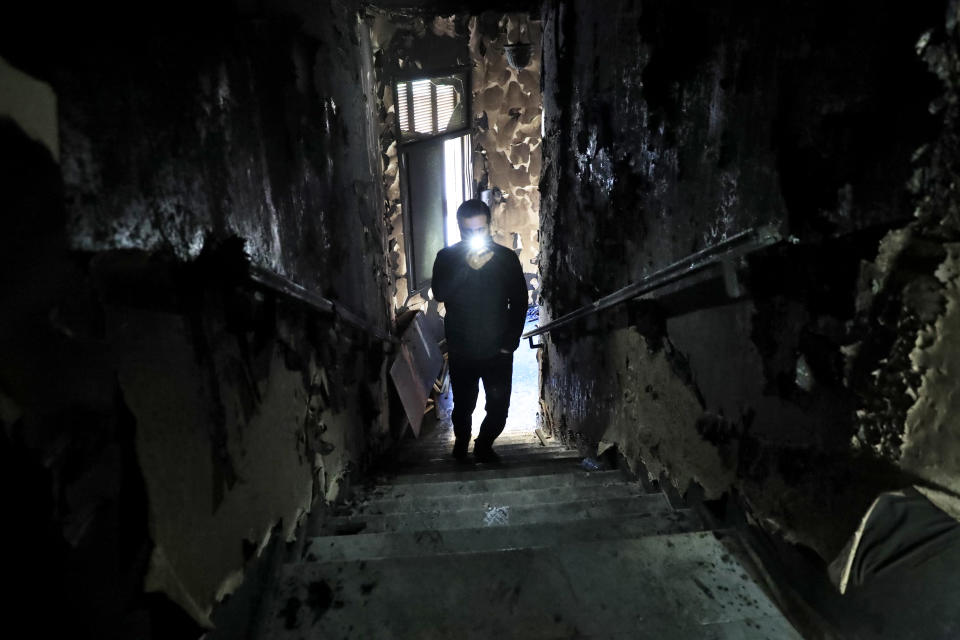 A man lights his mobile phone as he films the burned stairs of Tripoli municipality that was set on fire by protesters Thursday night, during a protest against deteriorating living conditions and strict coronavirus lockdown measures, in Tripoli, Lebanon, Friday, Jan. 29, 2021. (AP Photo/Hussein Malla)
