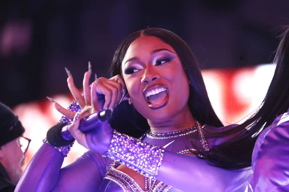 Megan Thee Stallion performs energetically on stage, seen mid-song with long, intricate nails and sparkling, embellished attire