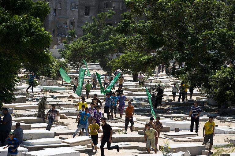 Palestinian children run with Hamas flags between tombs in the Beit Lahia cemetery in the northern Gaza Strip as they lead the funeral procession for the wife and seven-month-old son of Hamas's military commander Mohammed Deif on August 20, 2014