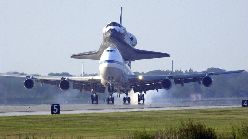 A 747 jet carries the space shuttle to an airport runway