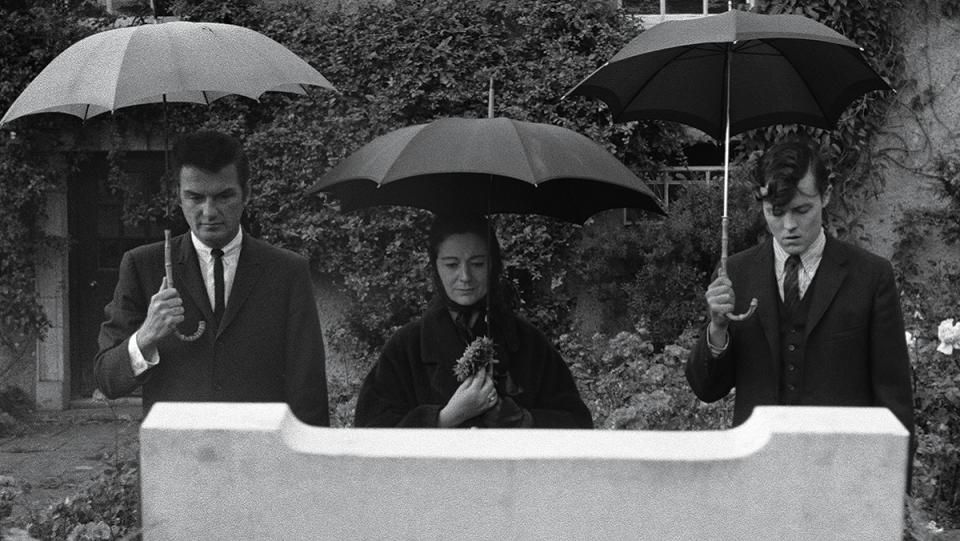 William Campbell and Bart Patton flank Eithne Dunne, each holding an umbrella, looking at a grave in Francis Ford Coppola's Dementia 13.