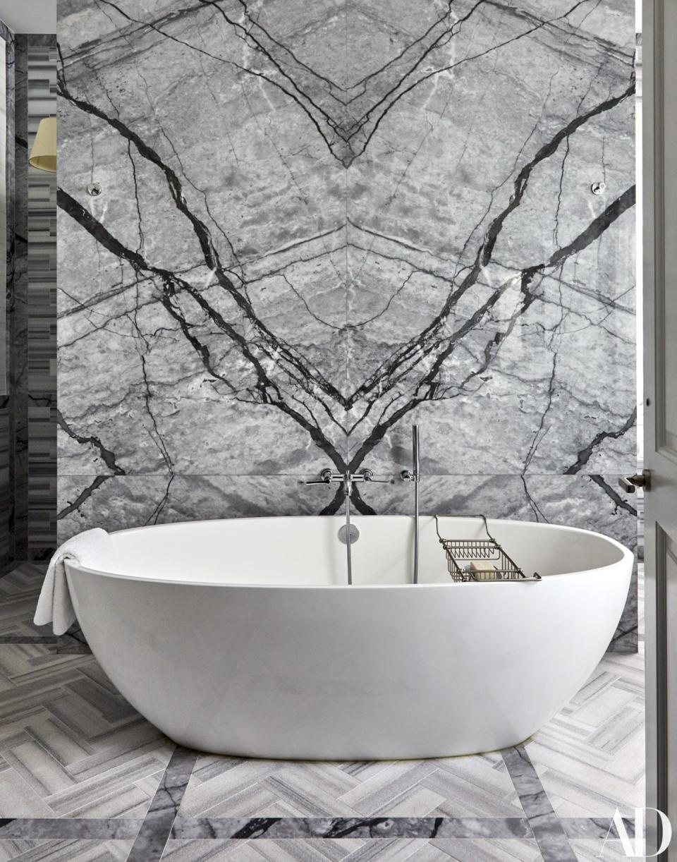 In the master bath, a Victoria + Albert tub with Rohl fittings stands in front of a Grigio Astratto stone wall. The herringbone tile floor is by Zebrino.