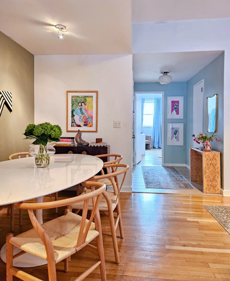 Dining room with one gray accent wall with statement art piece, oval white table with wood and rattan chairs, View into blue entryway