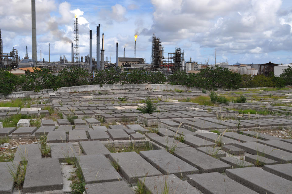 In this Nov. 12, 2012 photo, tombs in the Beth Haim cemetery are back dropped by the Isla oil refinery in Blenheim, on the outskirts of Willemstad, Curacao. Beth Haim, believed to be one of the oldest Jewish cemeteries in the Western Hemisphere, established in the 1950s and considered an important landmark on an island where the historic downtown has been designated a UNESCO World Heritage Site, is slowly fading in the Caribbean sun. Headstones are pockmarked with their inscriptions faded, stone slabs that have covered tombs in some cases for hundreds of years are crumbling into the soil, marble that was once white is now grey, likely from the acrid smoke that spews from the oil refinery that looms nearby. (AP Photo/Karen Attiah)