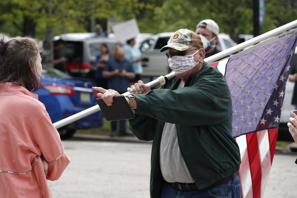 A man holding a flag engages with a counter-protester as people with ReopenNC gather in Raleigh, N.C., to press Gov. Roy Cooper to allow businesses to reopen during the COVID-19 outbreak Tuesday, April 21, 2020. (AP Photo/Gerry Broome)