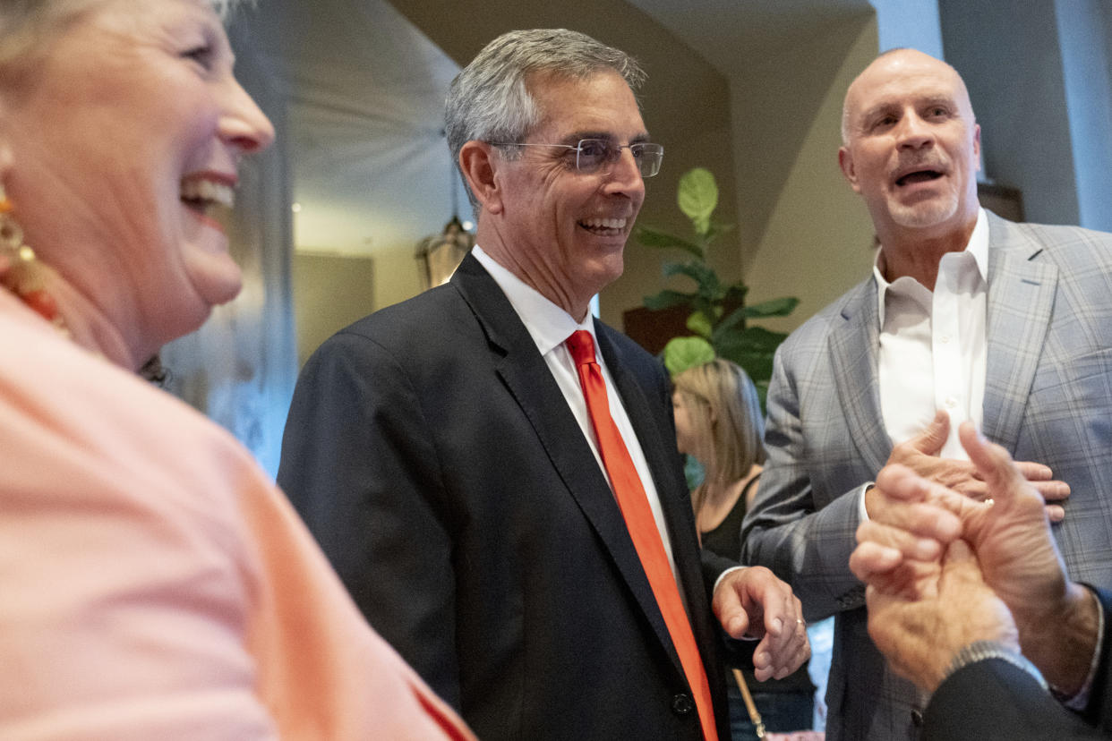 Brad Raffensperger and his wife, Tricia, stand and smile near others.