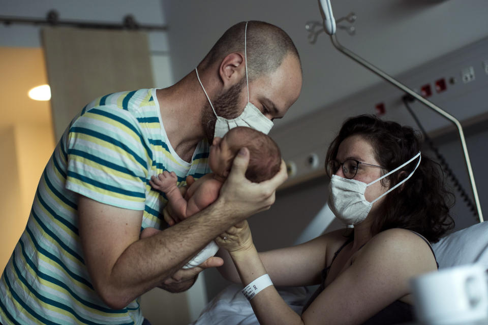 Cedric Dols, left, brings his newborn daughter, Anouk, to her mother, Marie L'Hoest, to be breastfed at the MontLegia CHC hospital in Liege, Belgium, Friday, June 26, 2020. Belgium has lifted most of its restrictions but still requires face masks on public transport and asks people to still keep a physical distance from each other, to prevent the spread of the COVID-19 coronavirus. (AP Photo/Francisco Seco)