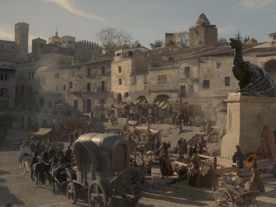 A scene from "House of the Dragon," showing a carriage going through a busy town square.