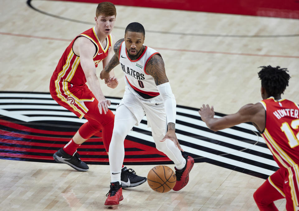 Portland Trail Blazers guard Damian Lillard, center, dribbles past Atlanta Hawks guard Kevin Huerter, left, during the first half of an NBA basketball game in Portland, Ore., Saturday, Jan. 16, 2021. (AP Photo/Craig Mitchelldyer)