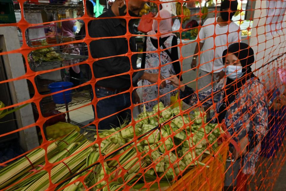 People wearing face masks amid concern over the spread of the COVID-19 coronavirus buy traditional delicacies, a custom ahead of Eid al-Fitr which marks the end of the Muslim holy month of Ramadan, at the Geylang Serai market installed with crowd control screen in Singapore on May 21, 2020. (Photo by Roslan RAHMAN / AFP) (Photo by ROSLAN RAHMAN/AFP via Getty Images)