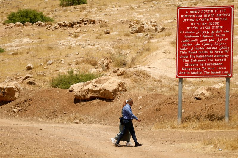 FILE PHOTO: Palestinians walk past a sign with information on Area "A" in Jordan Valley in the Israeli-occupied West Bank