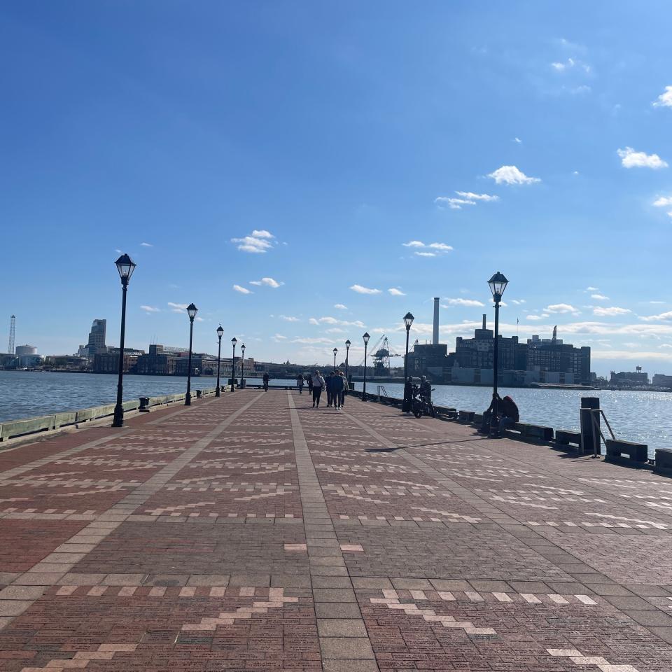 People walking on a boardwalk by the water with lampposts and a clear sky