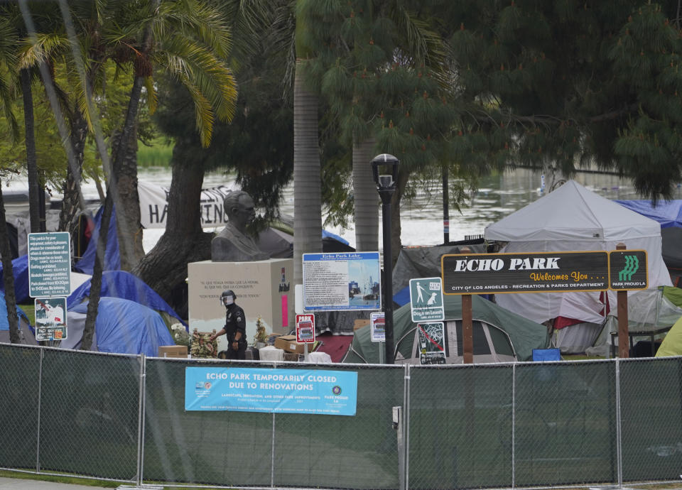 A Los Angeles Police officer walks under the Cuban national hero statue of Jose Marti, surrounded by homeless tents, inside Echo Park Lake's closed perimeter in Los Angeles, Thursday, March 25, 2021. A newly installed fence surrounded the park Thursday after a late-night confrontation between police and vocal demonstrators who oppose the city's effort to remove a large homeless encampment and perform extensive repairs of the site. People who were already in tents at Echo Park Lake were allowed to remain overnight but were given 24-hour notice to leave, Police Chief Michel Moore said in a social media post. (AP Photo/Damian Dovarganes)