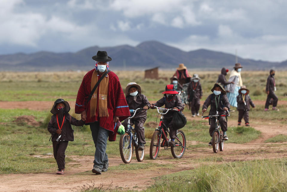 FLE - In this Feb. 4, 2021 file photo, Aymara Indigenous parents walk their children wearing new, protective uniforms to Jancohaqui Tana school as they return for their first week of in-person classes amid the COVID-19 pandemic, near Jesus de Machaca, Bolivia. According to Bolivia's Urban Teacher's Federation, they estimate that between 30% and 40% of students have deserted classes because of the lack of internet access during the pandemic. (AP Photo/Juan Karita, File)