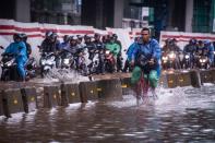 A cyclist rides alongside motorcyclists along a flooded street in Jakarta