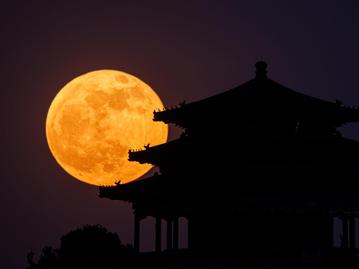 An image of the moon, against the silhoutte of a Chinese pagoda