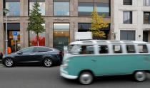 A Volkswagen oldtimer car drives past a Tesla Model X electric car recharging batteries in Berlin