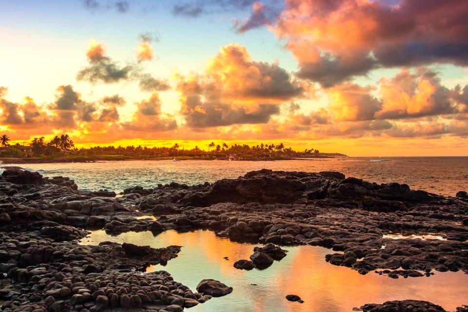 Sun setting over Kukuiula Bay, Kauai, Hawaii with clouds reflecting in the pool of water in the lava rocks