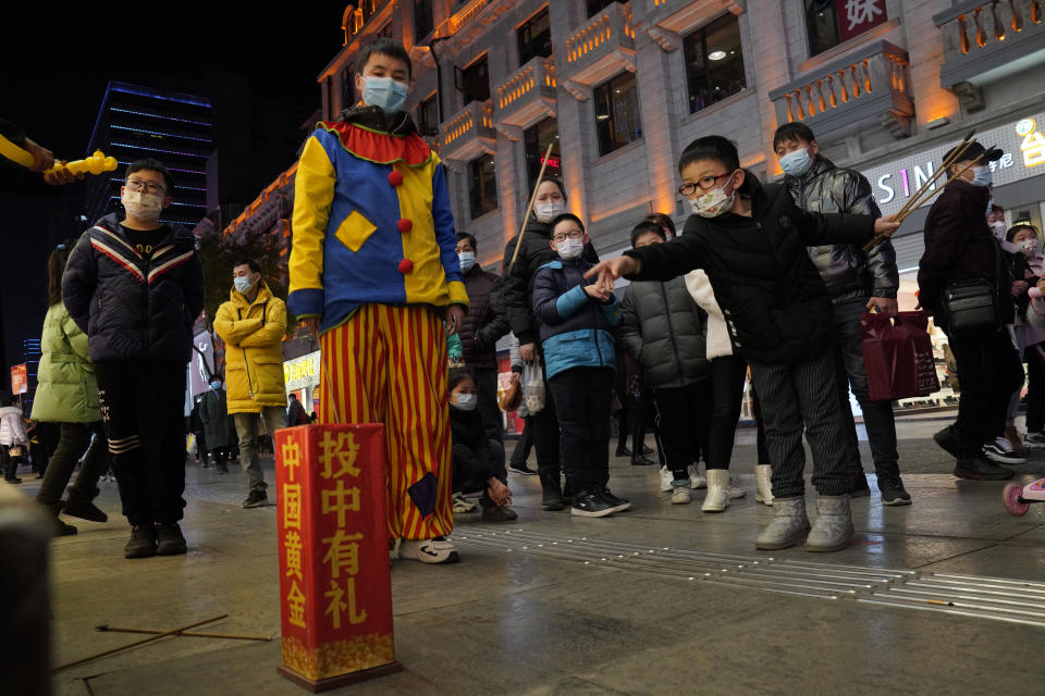 FILE - In this Jan. 15, 2021, file photo, a child attempts to throw sticks into a container to win prizes along a shopping street in Wuhan in central China's Hubei province. Couples go on dates, families dine out at restaurants, shoppers flock to stores. Face masks aside, people are going about their daily life pretty much as before in the Chinese city that was first hit by the COVID-19 pandemic. (AP Photo/Ng Han Guan, File)