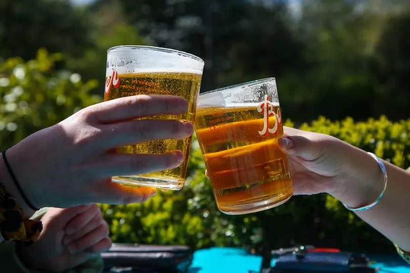 A couple raises their pints of beer on a warm sunny morning in a beer garden of a pub. (Stock image)