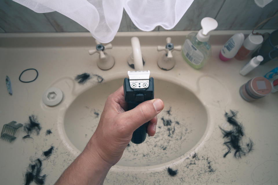 electric razor in someone's hand above the sink where hair has fallen