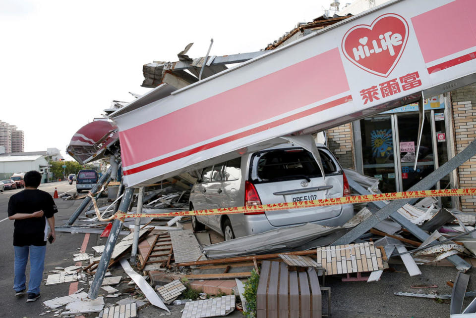 A man stands in front of a damaged vehicle and convenience store