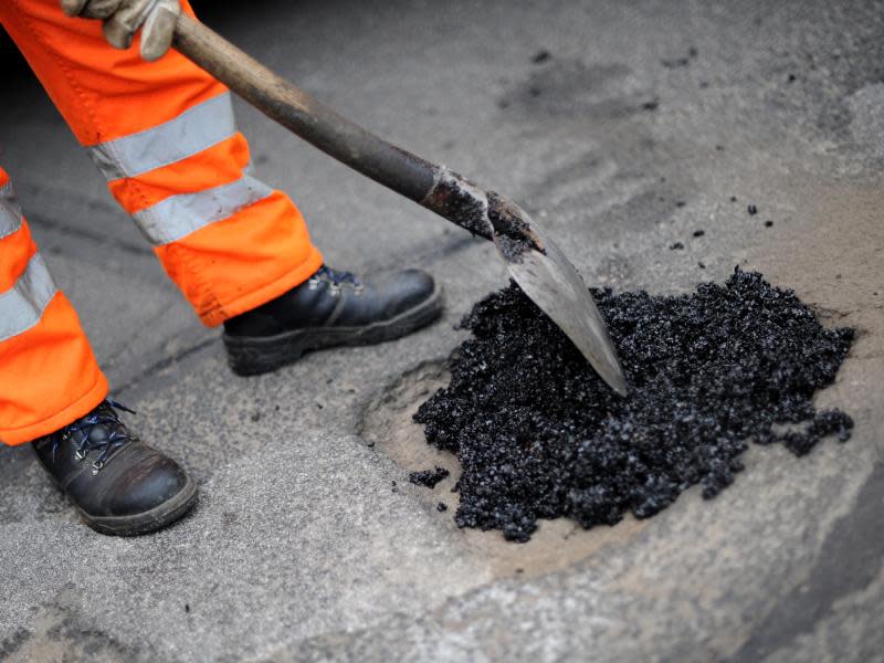 Ein städtischer Arbeiter füllt ein Schlagloch mit Asphalt. Foto: Uwe Zucchi/Archiv