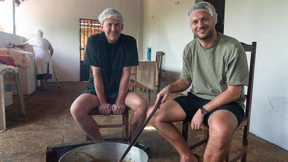 Scott and Sam stir a pot of fruit cooking over an open fire