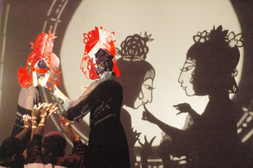 In relief: A picture of performers presenting a wayang-style performance of Larry Reed. The audience sits on the other side of the screen.