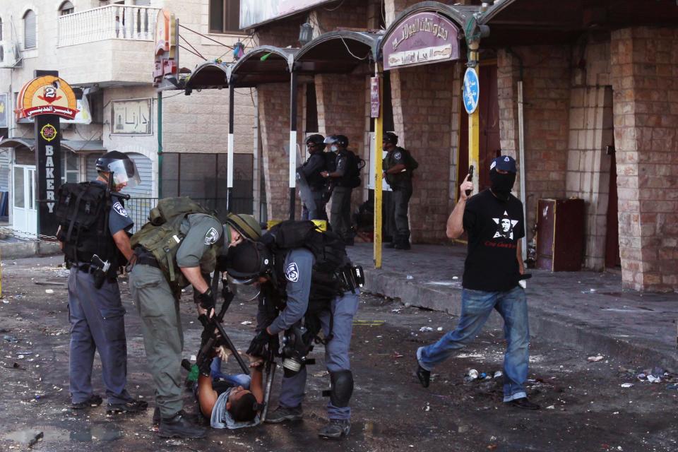 Israeli border policemen detain Palestinian protester as undercover Israeli policeman walks by during clashes following Friday prayers at Shuafat refugee camp in the West Bank