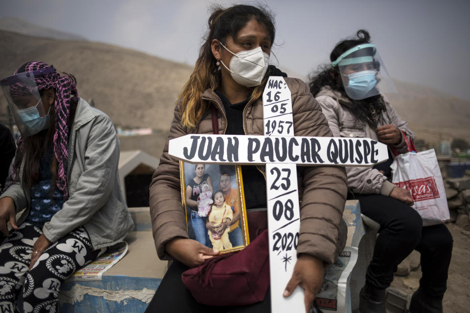 Ruth Morales, 36, center, waits for the arrival of the coffin of her husband, Juan Paucar Quispe, 63, who died from COVID-19 complications, during his burial at a cemetery in Carabayllo, Lima, Peru, Tuesday, Aug. 25, 2020. (AP Photo/Rodrigo Abd)