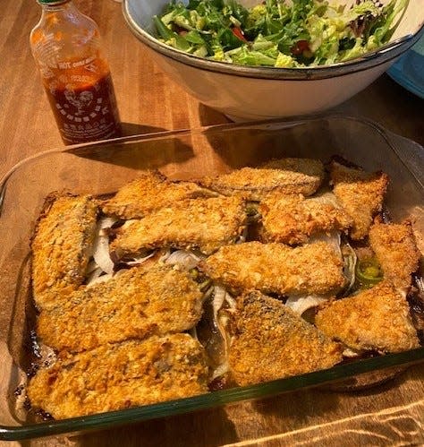 Marco Pompano showing off some baked pompano, encrusted with corn chips and topped with jalapeno capers and onions, and topped with lime sauce and sriracha.