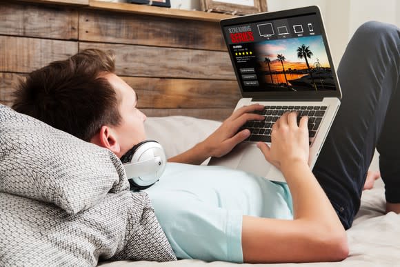 Man lying on a bed and watching a streaming series on a laptop computer