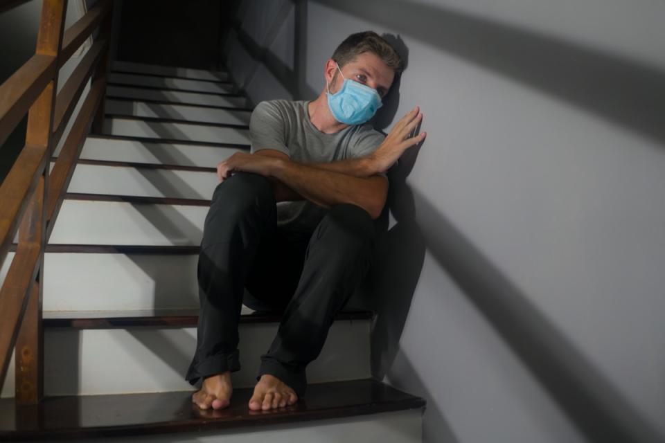 worried man in protective mask sitting on stairs at home staircase during lockdown and quarantine for covid-19