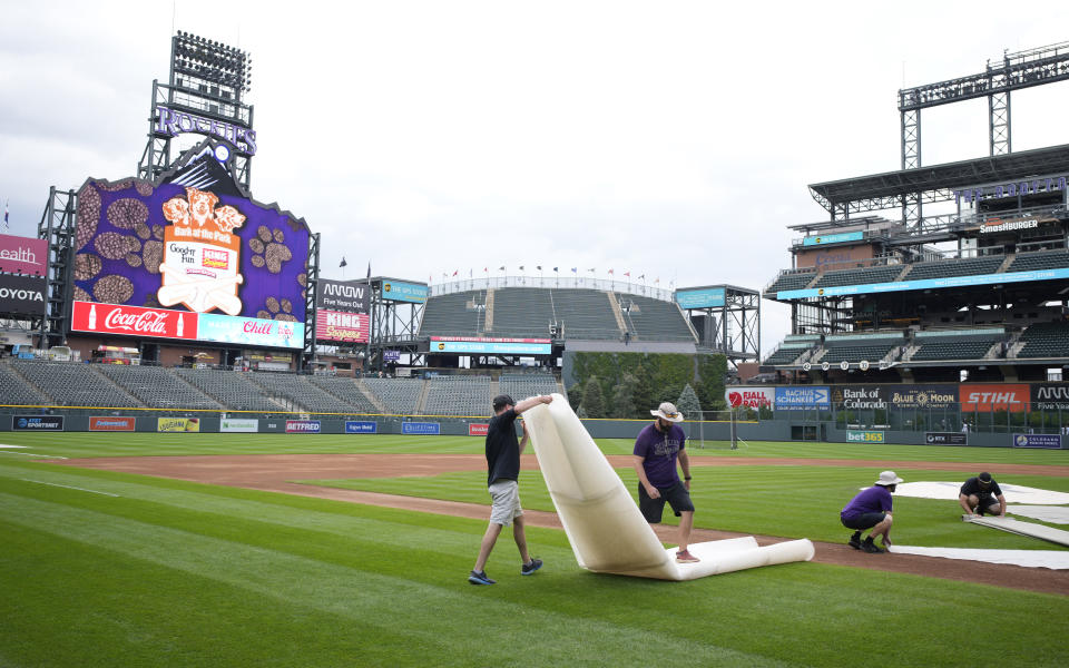 Grounds crew members pick up covers from the field after the postponement of a baseball game between the Colorado Rockies and the San Francisco Giants on Thursday, Sept. 14, 2023, in Denver. The game has been rescheduled as part of a doubleheader Saturday. (AP Photo/David Zalubowski)