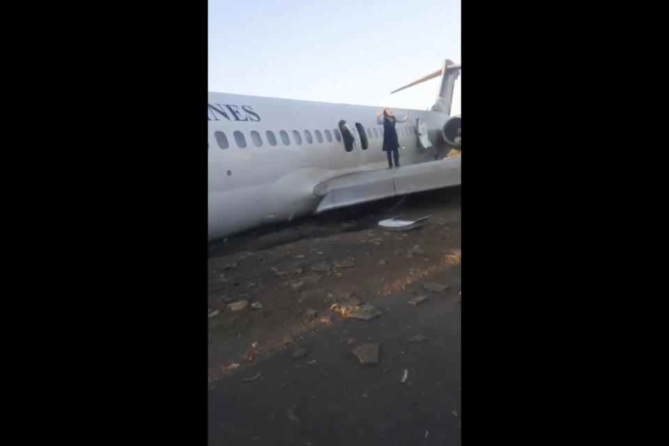 In this image from video shot by Iran's Civil Aviation Network News, a flight attendant shouts at onlookers as passengers walk off over the wing of a crashed plane in Mahshahr, Iran, Monday, Jan. 27, 2020. The Iranian passenger airliner carrying some 150 passengers skidded off the runway and into a street next to the airport in the southern city of Mahshahr on Monday, after apparently losing its landing gear in a hard landing. (Iran's Civil Aviation Network News via AP)