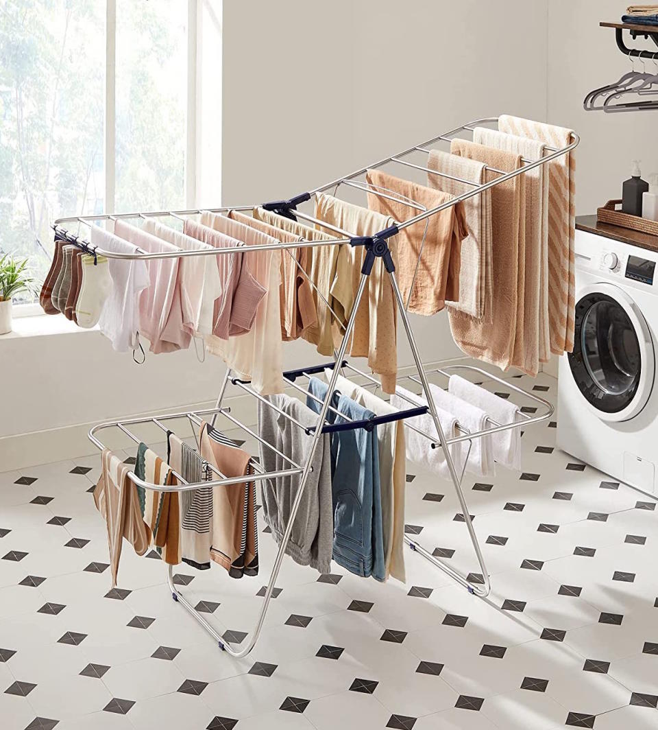 Songmics large drying rack with T-shirts  hanging in a laundry room that has black and white tiled floor