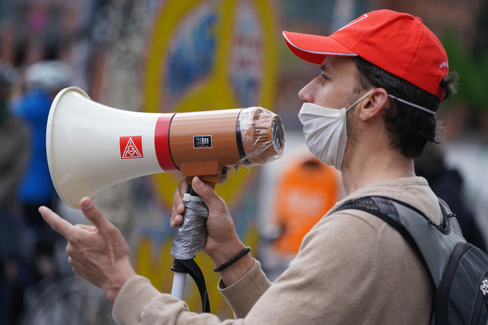 BERLIN, GERMANY - MAY 01: A member of the IG Metall labor union wears a protective face mask as he speaks into a megaphone covered with plastic wrap at a demonstration on May Day at Potsdamer Platz during the novel coronavirus crisis on May 1, 2020 in Berlin, Germany. May Day protests are taking place across Germany today, though as gatherings are limited by authorities to a maximum of 20 people per gathering due to coronavirus lockdown measures, many small protests are taking place instead of traditional, large-scale marches. (Photo by Sean Gallup/Getty Images)