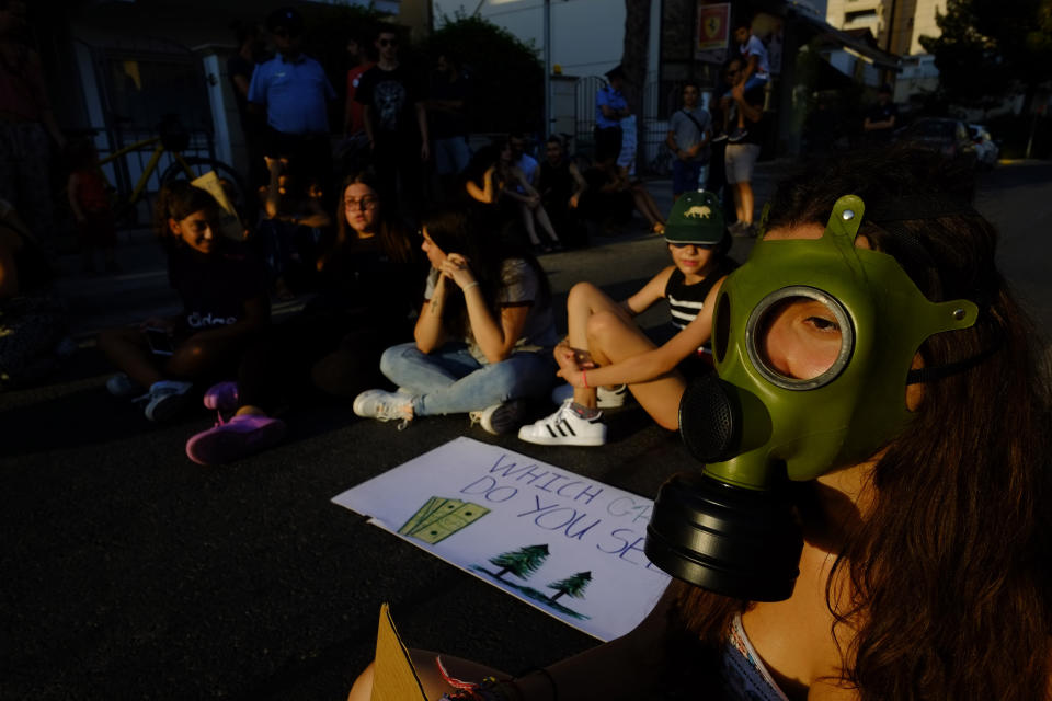 A woman in a mask with other protesters, block the road as they sit outside of the Brazilian Embassy during a protest in Nicosia, Cyprus, Friday, Aug. 23, 2019, Some people gathering outside of the Brazilian embassy to call on Brazil's President Jair Bolsonaro to act to protect the Amazon rainforest. The European Union is throwing its weight behind French President Emmanuel Macron's call to put the Amazon fires on the agenda of this weekend's G-7 summit of world leaders in France. (AP Photo/Petros Karadjias)